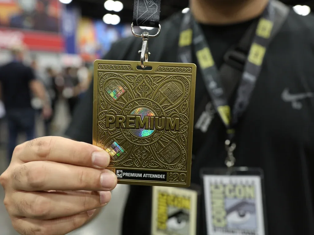 Premium Comic-Con badge with intricate design held by a fan, representing rising event costs.